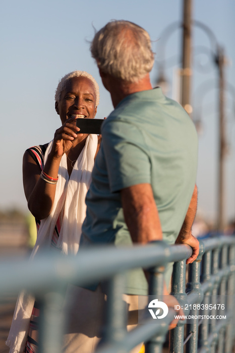 Senior woman photographing husband on sunny pier