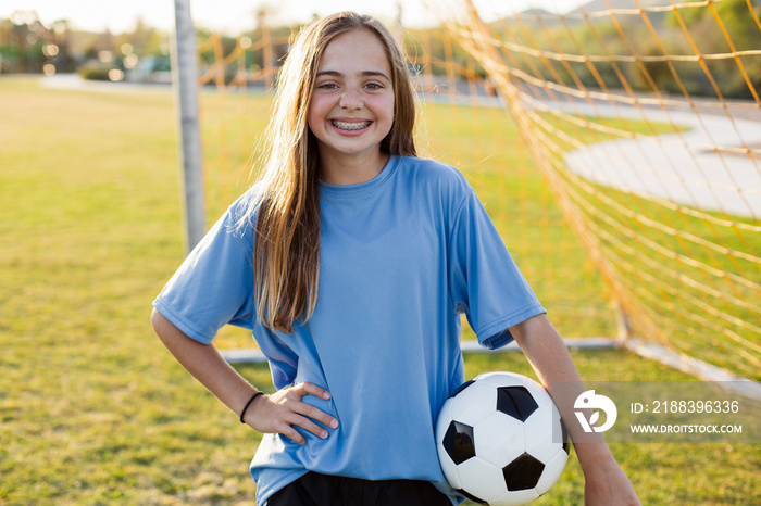 Portrait of smiling girl holding soccer ball in grassy field