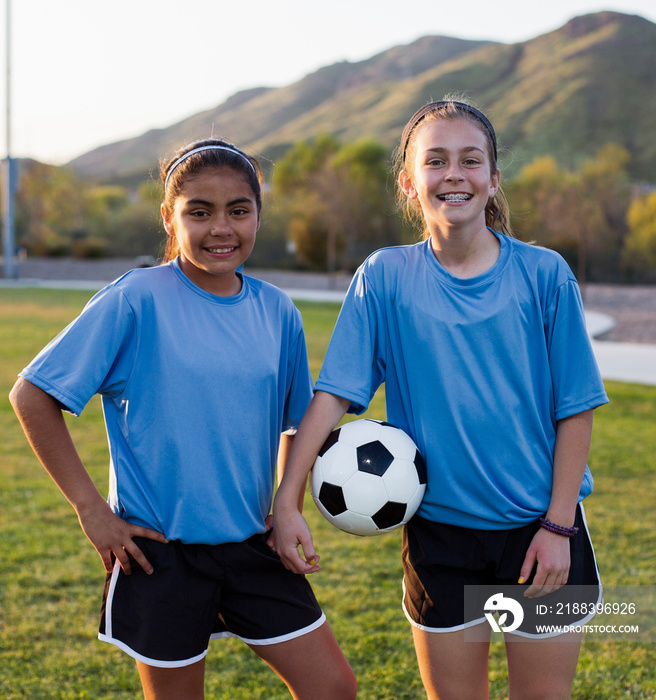 Portrait of smiling friends standing on soccer field against mountain during sunset