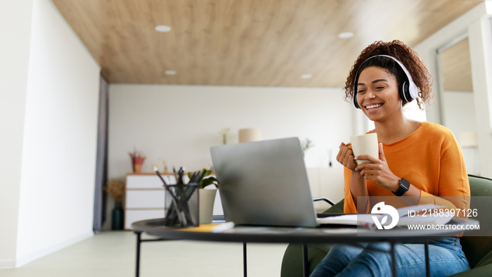 微笑的黑人女士在电脑上看视频，喝着热咖啡