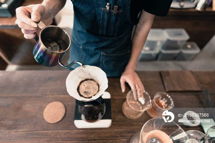 手滴咖啡，带蓝色围裙的咖啡师将热水倒在带过滤器的烤咖啡上。