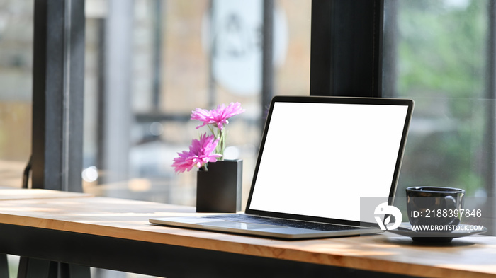 Open blank screen laptop computer in comfortable workspace with flower pot.