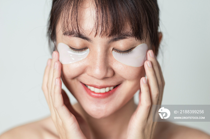 Asian woman smiling and applying patches mask under eyes for anti wrinkles and eye dark circles on f