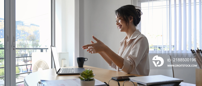 Cheerful businesswoman using laptop computer making video conference with her business partner at her workplace.