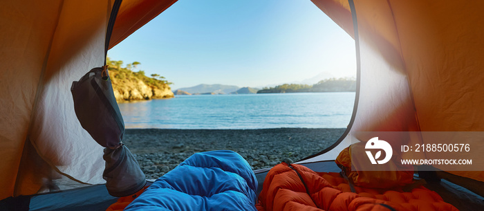 Two people travelers lying in tent in sleeping bags with view at wild tropical beach, wanderlust and adventure concept