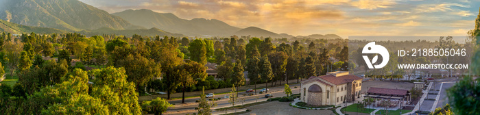 Landscape Southern California Valley with mountains,,  and trees lining avenues and church and cars in urban setting at sunset.