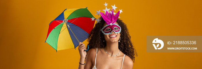 Young curly hair woman celebrating the Brazilian carnival party with Frevo umbrella on yellow.