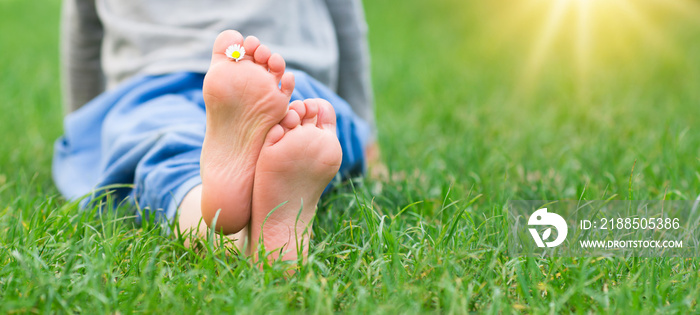 Kid foot on green grass on garden. Barefoot concept, freedom, relax and healthy feet. Panorama banner.