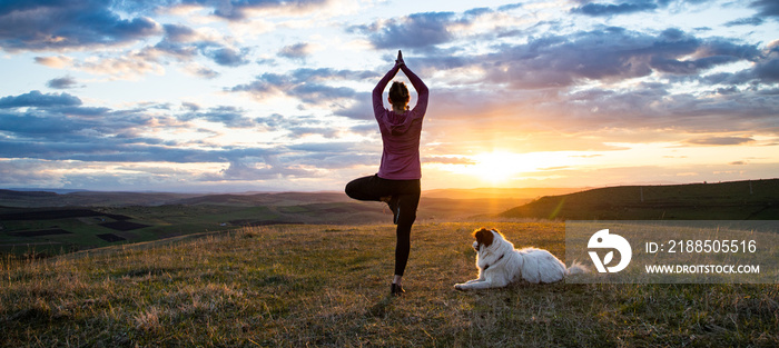 woman with white dog doing yoga at sunset tree pose  vrksasana