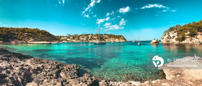 Panorama view of a beach bay with turquoise blue water and sailing boats and yachts at anchor with framed pine trees. Lovely romantic Cala Portals Vells, Mallorca, Spain. Balearic Islands