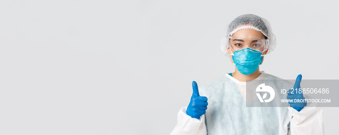 Covid-19, coronavirus disease, healthcare workers concept. Close-up of confident professional female asian doctor, tech lab employee in personal protective equipment show thumbs-up in approval