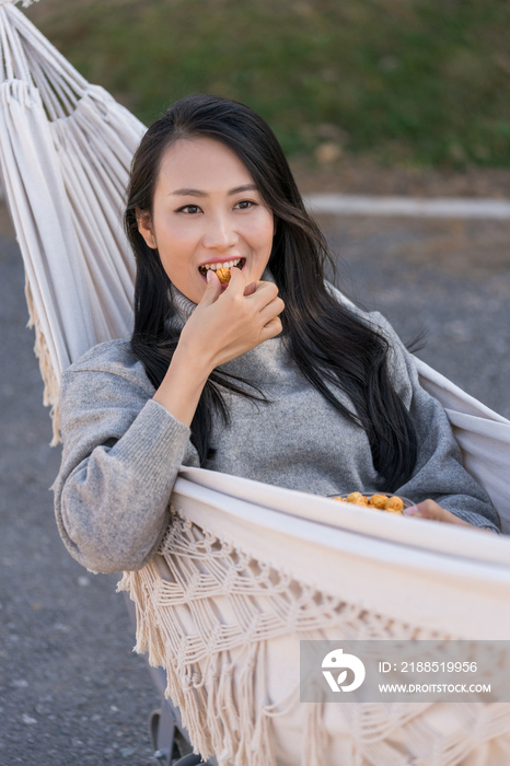 年轻女子坐在吊床上吃爆米花