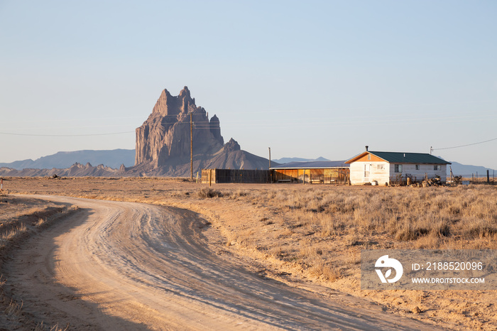 View of an old house in a dry desert with a Shiprock mountain peak in the background during a vibrant sunny sunrise.Taken at Rattlesnake, New Mexico, United States.