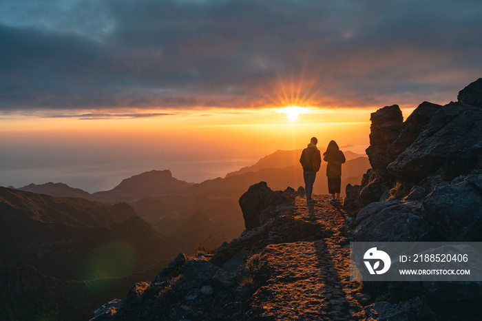 Happy young couple watching sunrise from the peak od Pico do Arieiro in Madeira. Silhouette of couple on the mountains. High quality photo