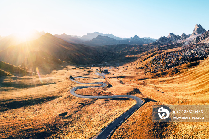 Fantastic aerial view on winding road in autumn mountain valley at sunset. The golden sunset light illuminates the mountains and orange grass. Passo Giau, Dolomite Alps, Dolomites, Italy