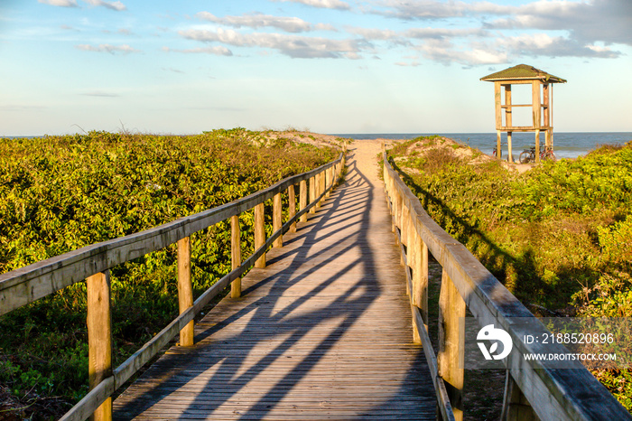 Lifeguard hut on Navegantes beach in the late afternoon, with wooden walkway over the dunes and native vegetation, blue sky with clouds, Navegantes, Santa Catarina