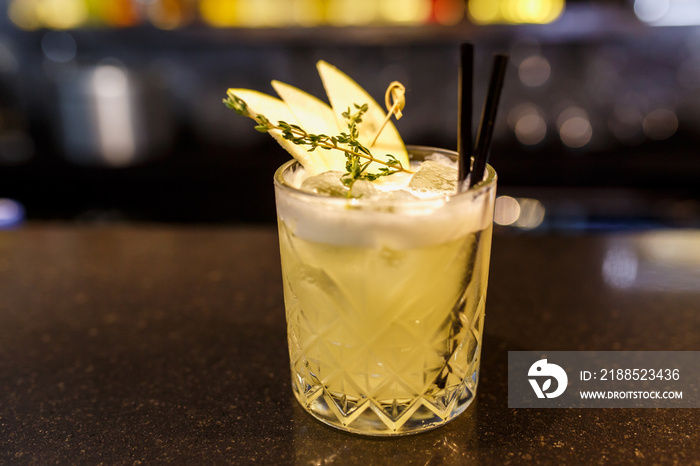 a glass of beautiful bright cocktail on a wooden surface decorated with fruits, berries, leaf of mint and basil at bar counter background