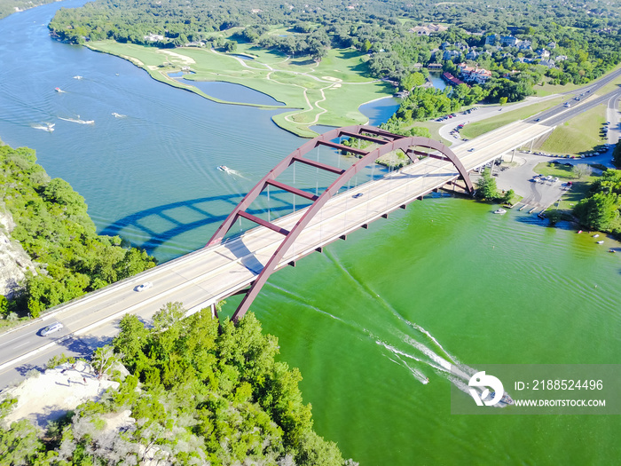 Aerial view Pennybacker Bridge or 360 Bridge, a landmark in Austin, Texas, US. Variety of high speed boat, yacht, jet ski on Colorado River and car traffic. Top of Town Lake and Hill Country landscape