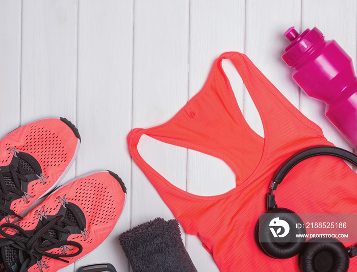 Fitness accessories including sneskers, top, bottle with water on the white wooden background