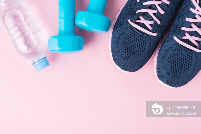 Female sport shoes, blue dumbbells and bottle of water on a pink background with copy space, top view