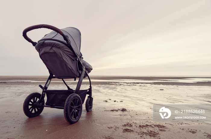 A infant baby childs stroller pushchair pram on a vast beach landscape at dusk and dawn. Relaxing and taking a holiday with children. Bonding travel with family in the great outdoors.