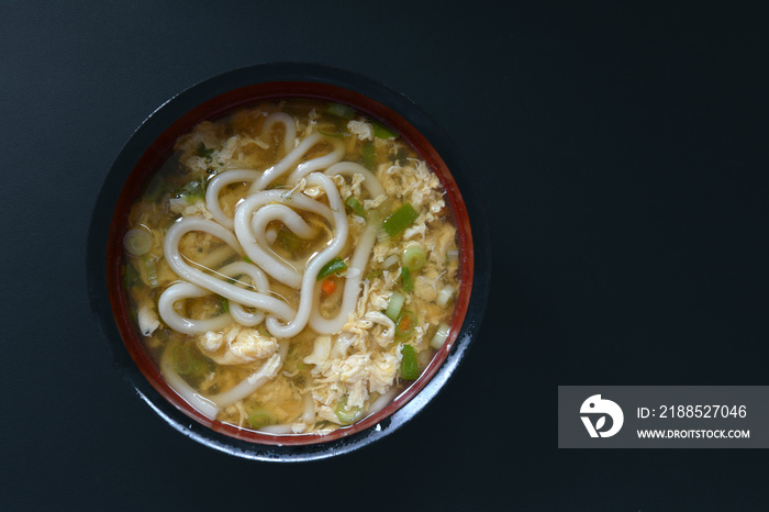 Top view of Japanese soup with traditional  ’Udon’ wheat flour noodle in ceramic pot on black background