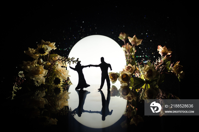 Silhouettes of toy couple dancing under the Moon at night. Figures of man and woman in love dancing at moonlight