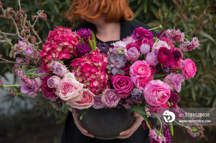 The florist holds beautiful composition of flowers in basket