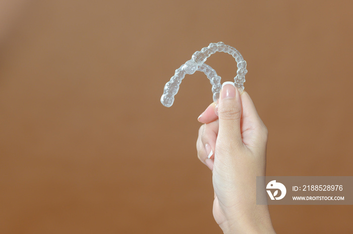 Close up young woman hand is holding Invisalign over brown background