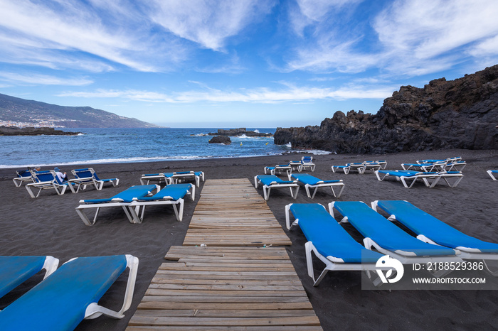 Blue sunbeds and black sand beach at Los Cancajos. La Palma, Canary Island, Spain.