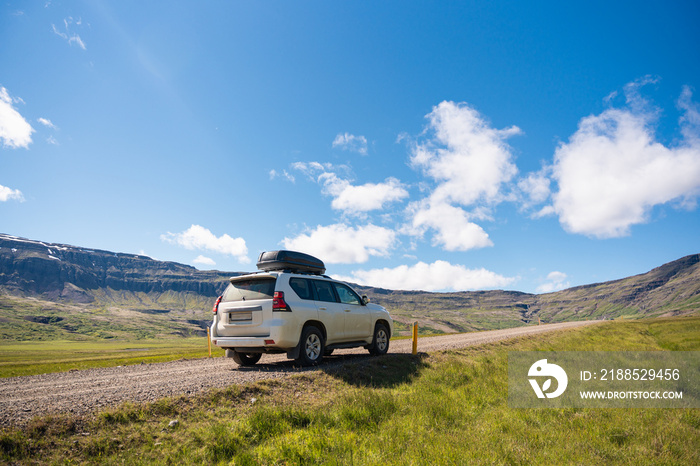 Large car parked on dirt road among the mountain and meadow on sunny day in summer