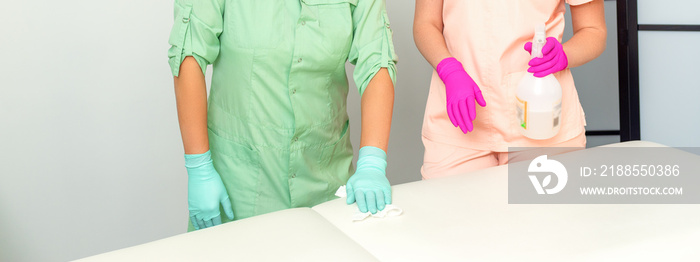 Two medical workers disinfect the patient’s couch with sanitizer spray and a clean napkin. Health and hygiene concept