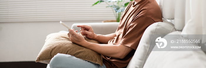 Technology Concept The man sitting next to a pot of plant, putting a small pillow on his lap, and checking something on his smartphone