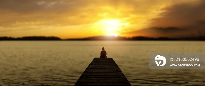 The man sitting on the dock with orange sunset sky along with lake scenery.
