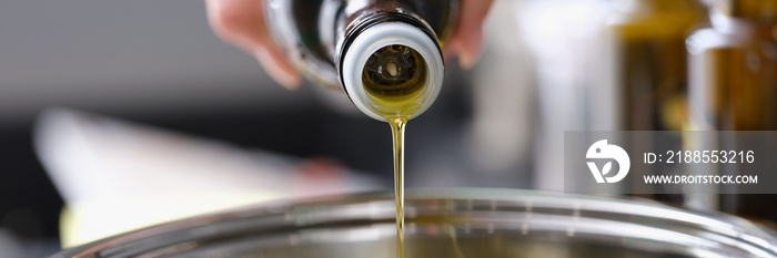 Olive oil is poured from a bottle into a saucepan