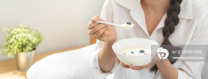 Healthy lifestyle, wellness food asian young woman hand use spoon eat tasty fresh organic yogurt, dairy product in bowl breakfast meal at home. Snack tasty on diet nutrition delicious natural yoghurt