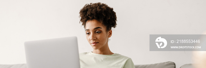 Young black woman working with laptop while sitting on couch at home