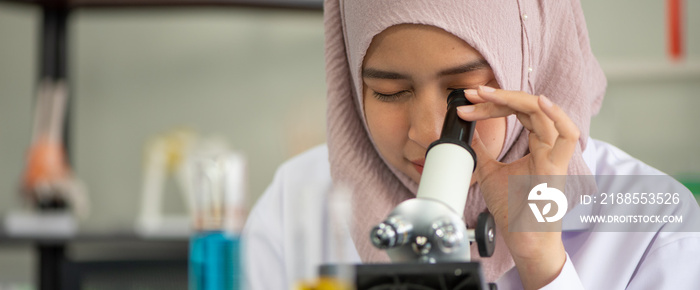 Young Muslim woman doctor looking on microscope in scientific laboratory research development education.