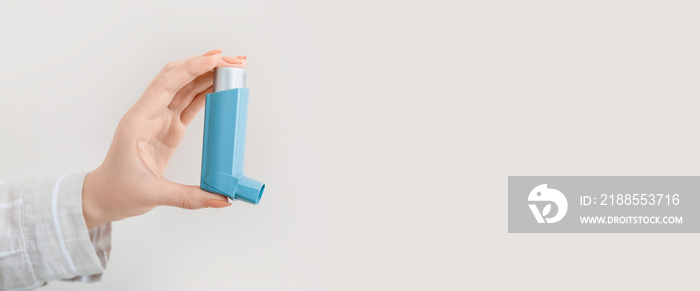 Female hand holding asthma inhaler on light background with space for text