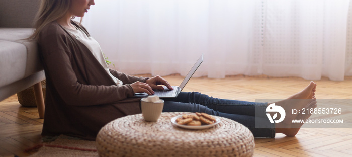 Young woman typing on laptop, resting on floor at home