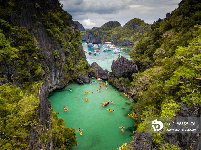 Aerial drone view of a beautiful tropical lagoon filled with kayaks and surrounded by jagged limestone cliffs (Small Lagoon, Miniloc Island, El Nido)