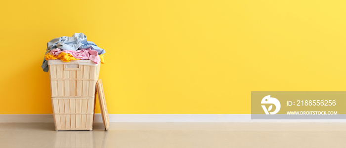 Wooden basket with laundry near yellow wall. Banner for design