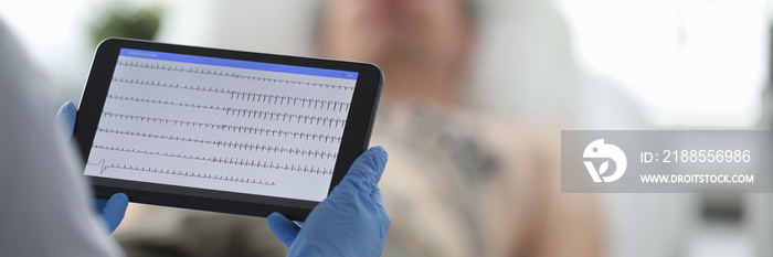 Doctor with ecg monitor stands in front of patient in background. Diagnosis of diseases of cardiovascular system concept.