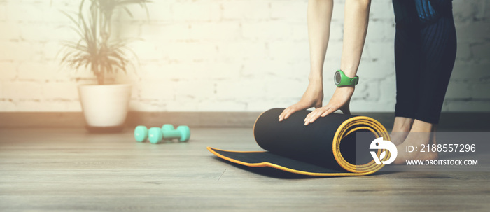 yoga practice or fitness workout at home. woman rolling exercise mat in room. banner copy space