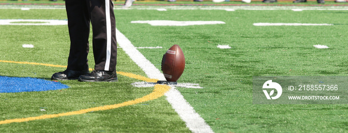 Football on the tee for kickoff with thr referee standing next to the ball