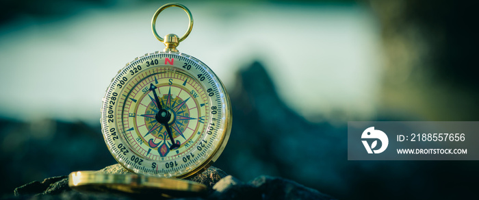 Analogical compass abandoned on the rocks with blurred sea background. Vintage tone. Cinema style