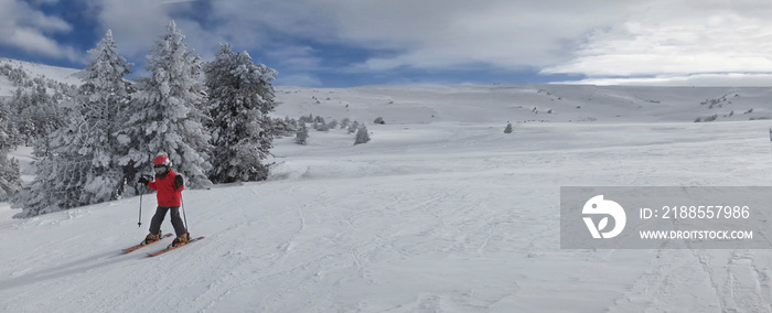 little boy in a red jacket, skiing in a winter resort in the Pyrenees with empty slopes, panoramic format, copy space on the right