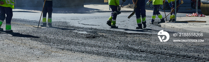 Panoramic view of professional workers from an asphalt company working with their shovels and brushes in the last phase of the application of the pavement layer on city streets.