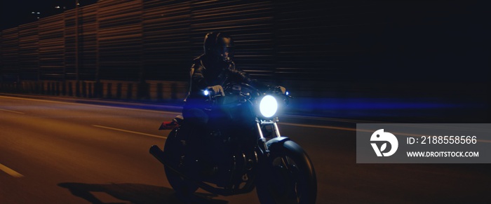 Biker riding his custom built cafe racer motorcycle through city at night. Shot with 2x anamorphic lens