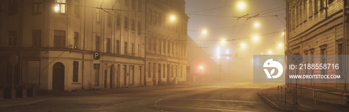 An empty illuminated asphalt road through the old historical buildings and houses in a fog at night. Street lights (lanterns) close-up. Riga, Latvia. Dark cityscape